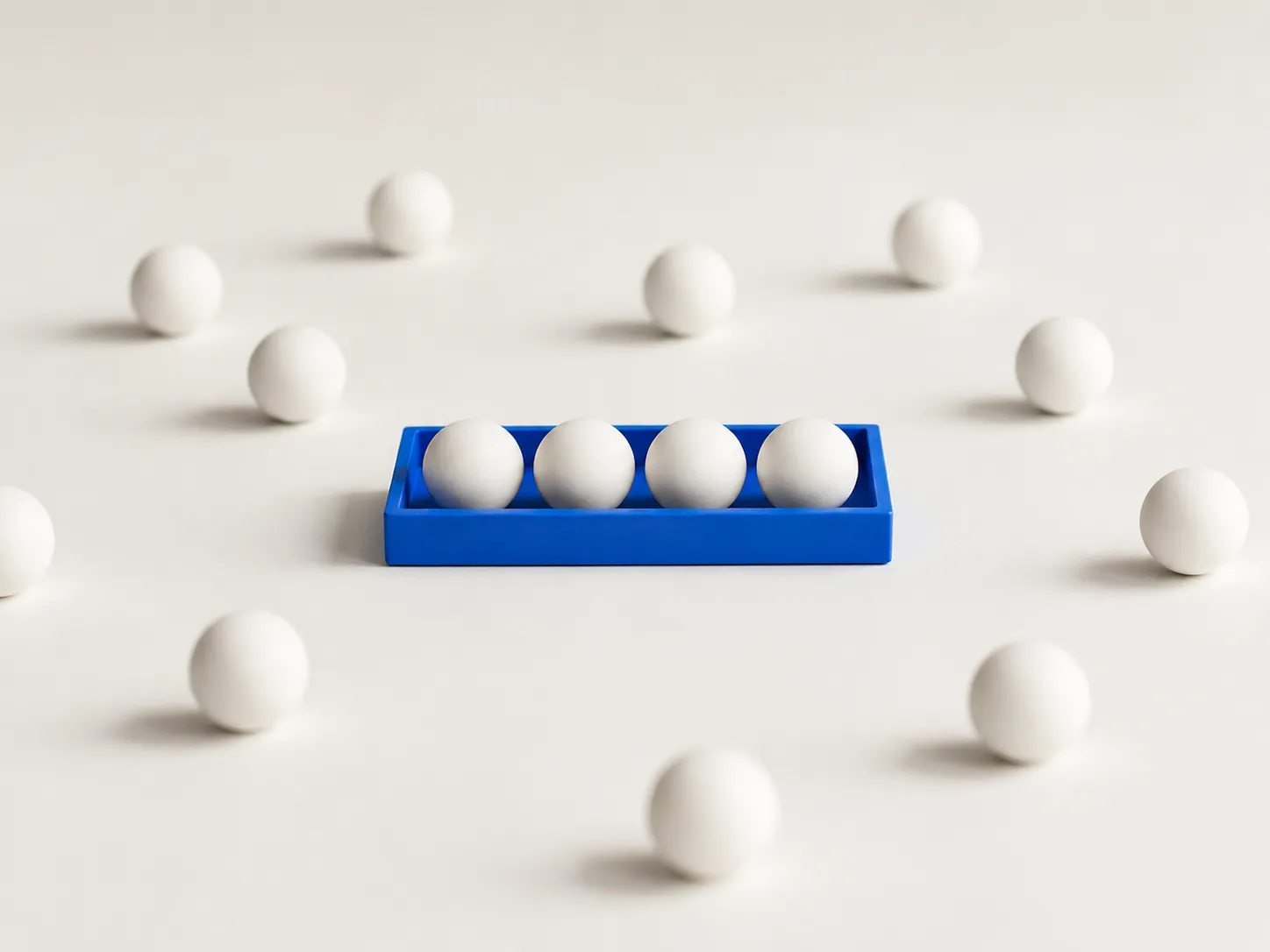 Four white spheres lined up in a blue tray, with loose white spheres scattered around on a light surface